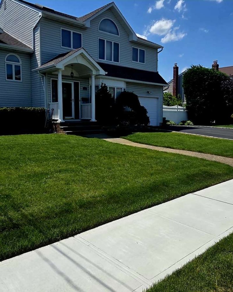 Healthy edged lawn alongside a clean concrete walkway in front of a colonial home